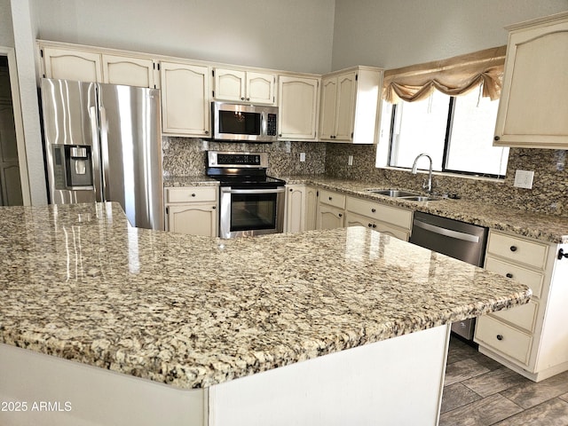 kitchen featuring light stone counters, cream cabinetry, stainless steel appliances, decorative backsplash, and a sink