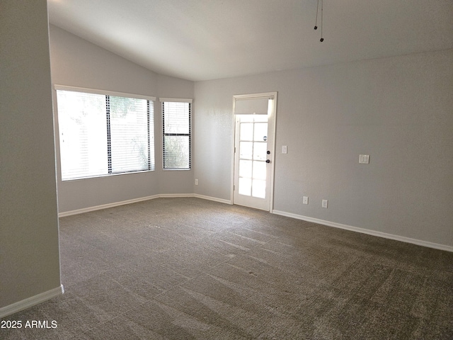 spare room with vaulted ceiling, dark colored carpet, and baseboards