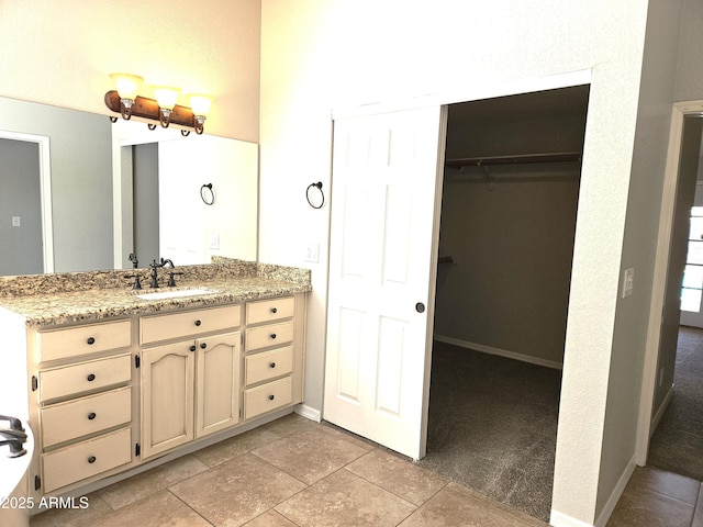 full bath with a walk in closet, vanity, and baseboards