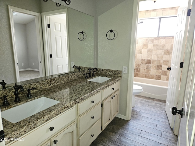 bathroom with toilet, wood tiled floor, double vanity, and a sink