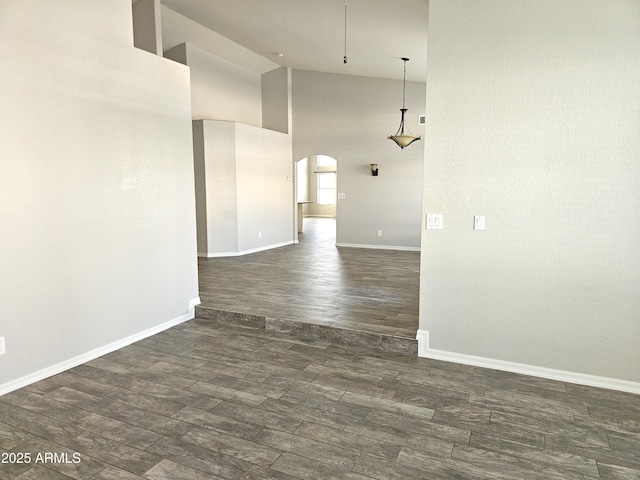 unfurnished room with arched walkways, high vaulted ceiling, dark wood-style flooring, and baseboards