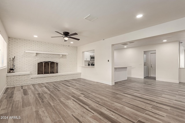 unfurnished living room with a fireplace, hardwood / wood-style floors, ceiling fan, and brick wall