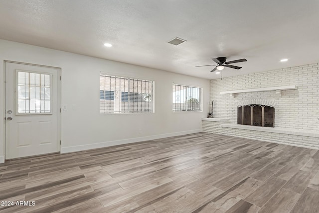 unfurnished living room featuring hardwood / wood-style floors, a healthy amount of sunlight, and a brick fireplace