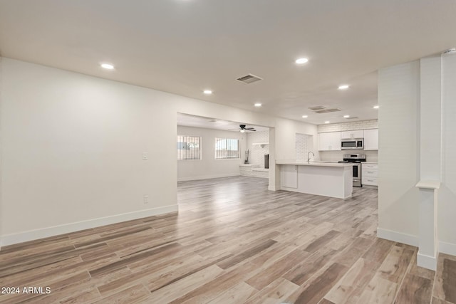 unfurnished living room featuring a fireplace, light wood-type flooring, ceiling fan, and sink