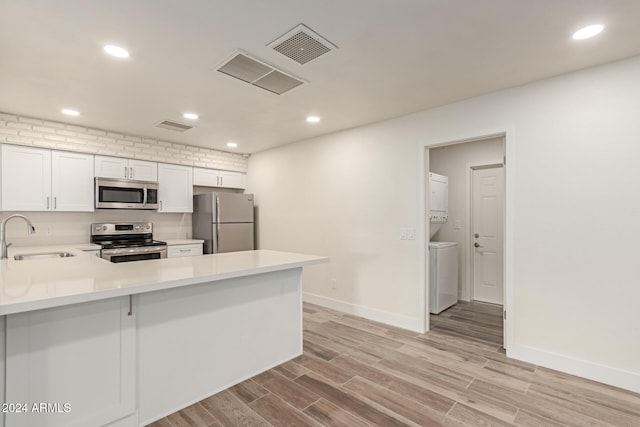 kitchen with sink, stainless steel appliances, kitchen peninsula, light hardwood / wood-style floors, and stacked washer / drying machine