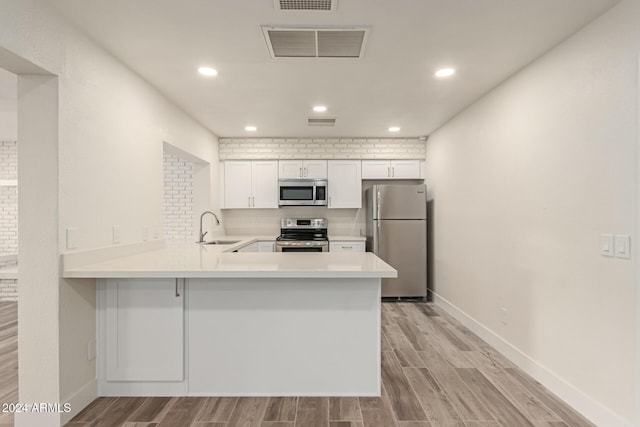 kitchen with kitchen peninsula, stainless steel appliances, white cabinets, and light hardwood / wood-style floors