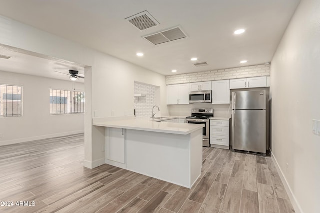 kitchen with kitchen peninsula, stainless steel appliances, white cabinets, and light hardwood / wood-style floors