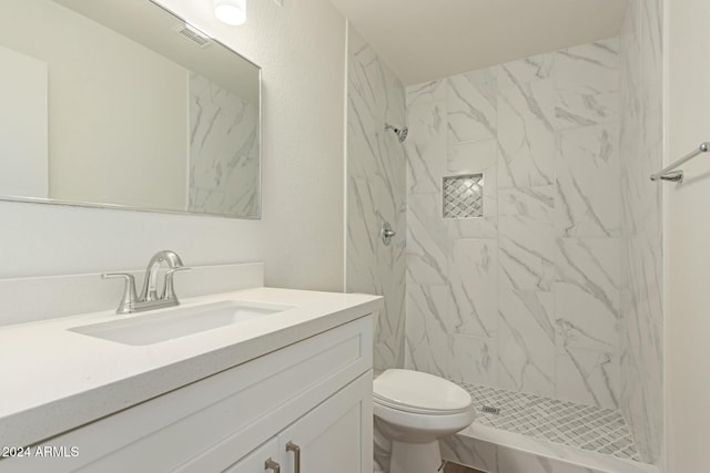 bathroom with tiled shower, vanity, and toilet