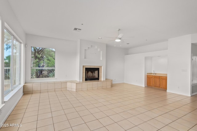 unfurnished living room with light tile patterned floors, a tile fireplace, visible vents, and ceiling fan