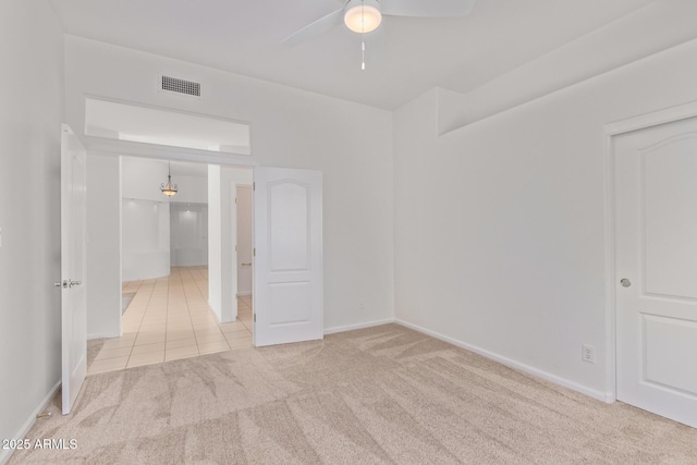carpeted empty room with tile patterned flooring, visible vents, a ceiling fan, and baseboards