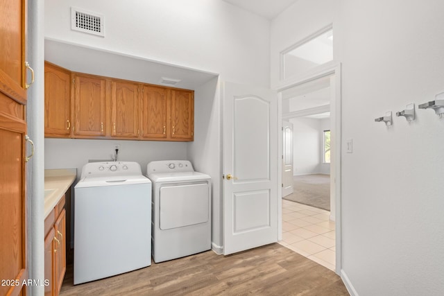 laundry area with light wood finished floors, visible vents, baseboards, washer and dryer, and cabinet space