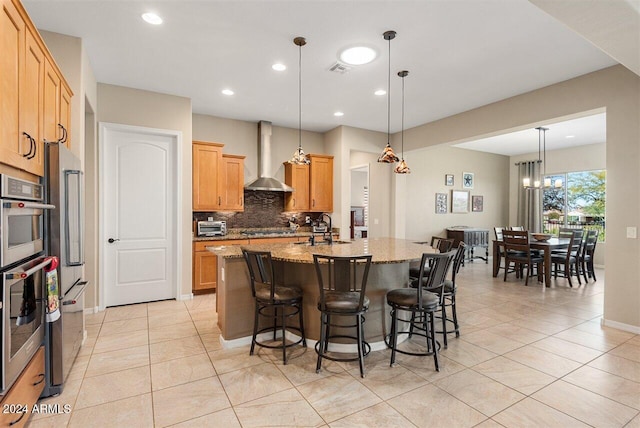 kitchen with light stone countertops, sink, wall chimney range hood, a notable chandelier, and decorative light fixtures