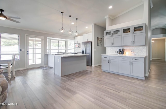 kitchen with a ceiling fan, a kitchen island, light countertops, appliances with stainless steel finishes, and tasteful backsplash