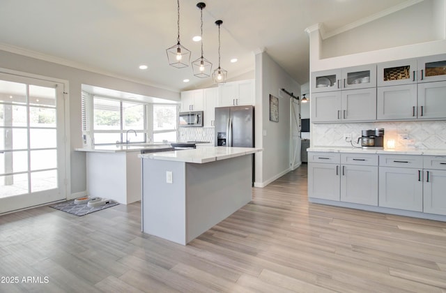 kitchen featuring light wood finished floors, backsplash, a kitchen island, crown molding, and appliances with stainless steel finishes