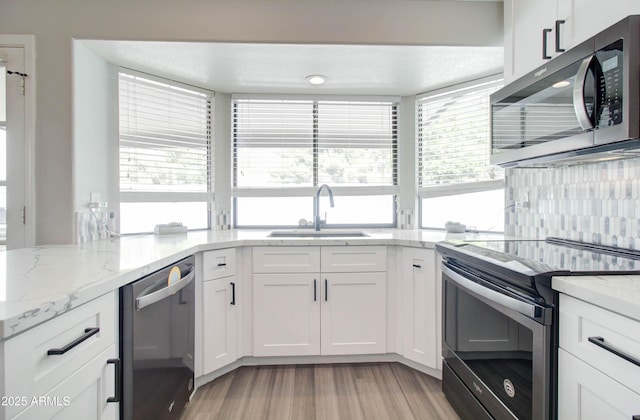 kitchen with light wood-style flooring, a sink, stainless steel appliances, white cabinets, and light stone countertops