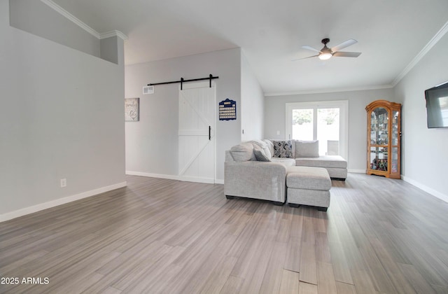 unfurnished living room featuring a ceiling fan, wood finished floors, a barn door, crown molding, and baseboards