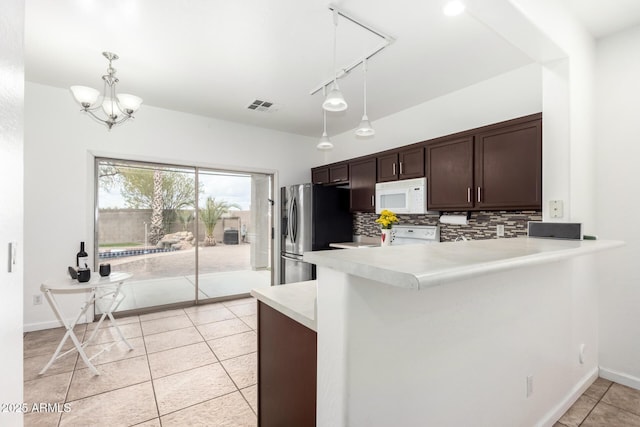 kitchen with stainless steel fridge, hanging light fixtures, dark brown cabinets, decorative backsplash, and kitchen peninsula