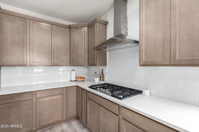 kitchen with light hardwood / wood-style floors, stainless steel gas stovetop, decorative backsplash, and wall chimney exhaust hood