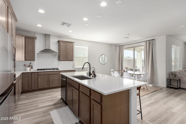 kitchen featuring a kitchen island with sink, wall chimney exhaust hood, light hardwood / wood-style flooring, and sink