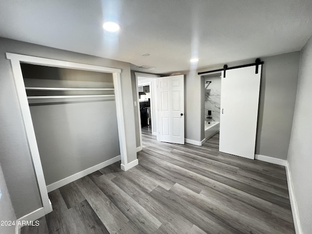 unfurnished bedroom with hardwood / wood-style flooring, a barn door, and a closet