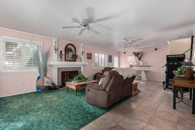 living area featuring light tile patterned floors, baseboards, a tiled fireplace, ceiling fan, and ornamental molding