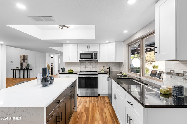 kitchen with white cabinets, stainless steel appliances, and a raised ceiling