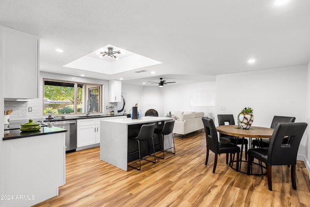 kitchen featuring white cabinets, stainless steel dishwasher, light hardwood / wood-style floors, a center island, and backsplash