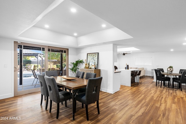 dining space with hardwood / wood-style floors, a tray ceiling, and a skylight