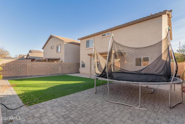 back of house featuring a trampoline, a lawn, and a patio