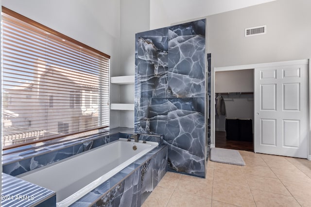 bathroom featuring a high ceiling, tile patterned floors, and a relaxing tiled tub