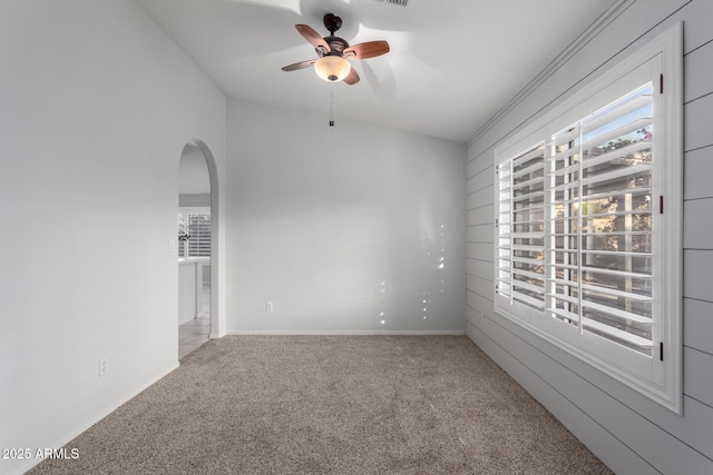 carpeted empty room featuring visible vents, arched walkways, lofted ceiling, and a ceiling fan