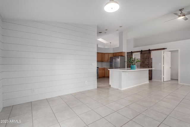 kitchen with freestanding refrigerator, a barn door, brown cabinetry, light countertops, and ceiling fan