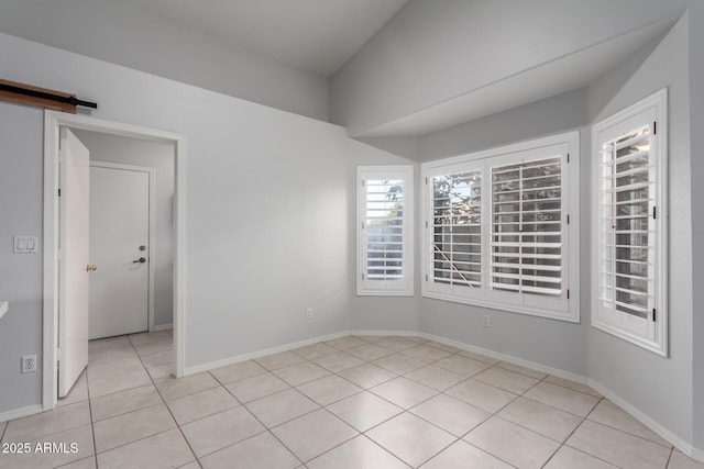 unfurnished room with a barn door, light tile patterned floors, and baseboards