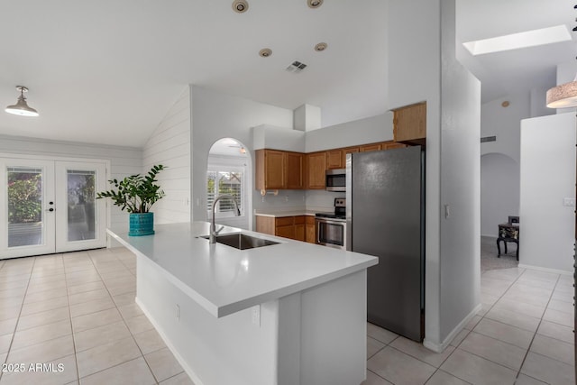 kitchen featuring visible vents, a sink, arched walkways, appliances with stainless steel finishes, and brown cabinetry