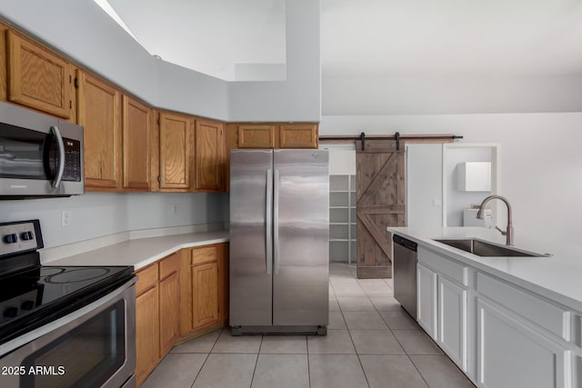 kitchen featuring light countertops, a barn door, appliances with stainless steel finishes, light tile patterned flooring, and a sink