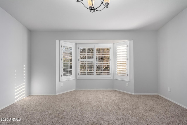 carpeted spare room with baseboards and an inviting chandelier