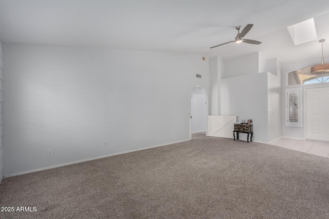 empty room featuring light colored carpet, a skylight, arched walkways, high vaulted ceiling, and a ceiling fan