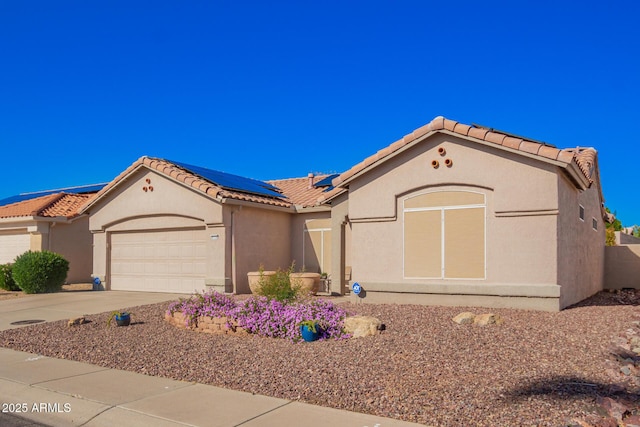 mediterranean / spanish home featuring a tiled roof, stucco siding, solar panels, and an attached garage