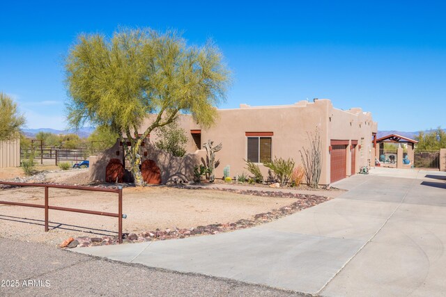 pueblo revival-style home with stucco siding, fence, driveway, and a garage