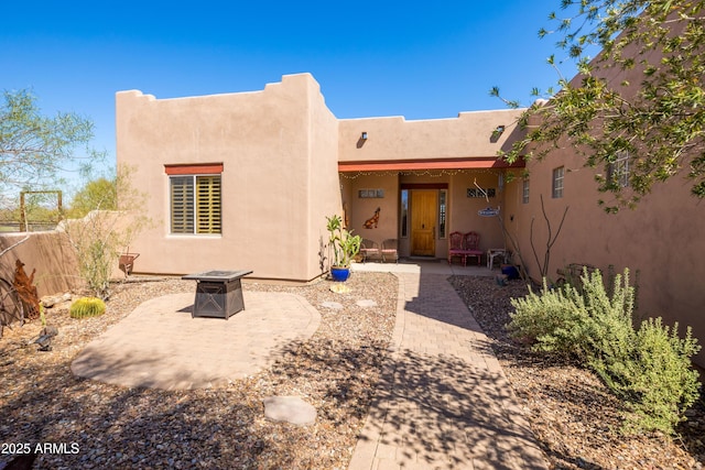 view of front of house featuring fence, a patio, an outdoor fire pit, and stucco siding