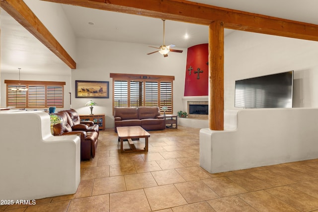 living area featuring a fireplace with raised hearth, a healthy amount of sunlight, a ceiling fan, and beamed ceiling