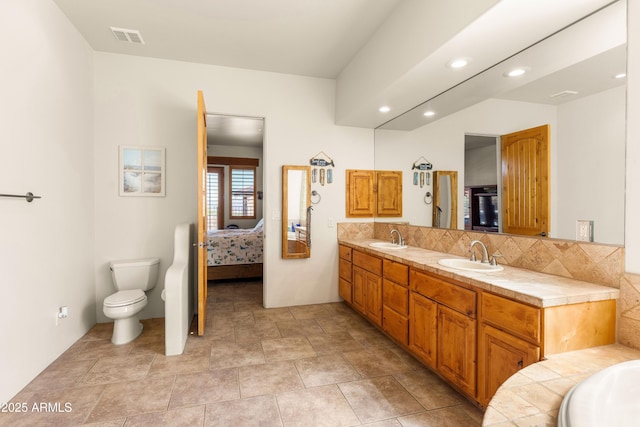 ensuite bathroom with double vanity, visible vents, toilet, and a sink
