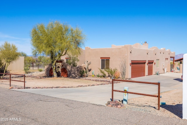 adobe home featuring stucco siding, an attached garage, concrete driveway, and fence
