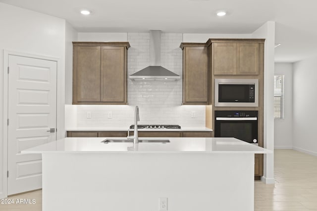 kitchen featuring wall chimney range hood, a sink, black oven, built in microwave, and tasteful backsplash