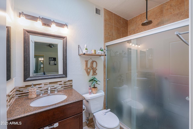 bathroom with toilet, vanity, backsplash, and a shower with door