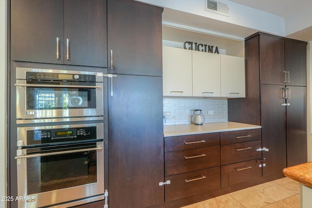 kitchen featuring double oven, backsplash, light tile patterned flooring, and white cabinetry