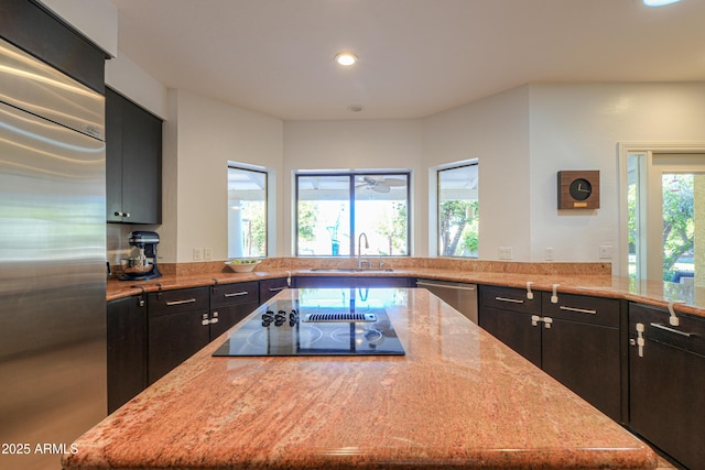 kitchen with a wealth of natural light, stainless steel appliances, light stone counters, and sink