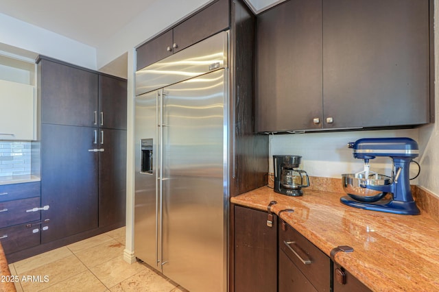 kitchen featuring light tile patterned floors, decorative backsplash, dark brown cabinets, and built in fridge