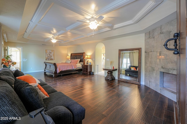 bedroom featuring dark wood-type flooring, ornamental molding, ceiling fan, a tile fireplace, and coffered ceiling