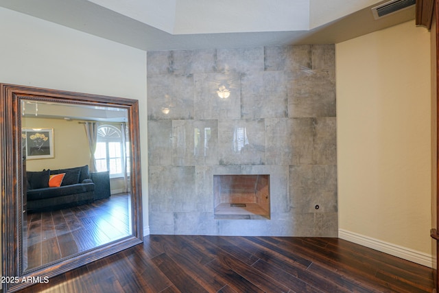 unfurnished living room featuring a tiled fireplace and dark hardwood / wood-style floors